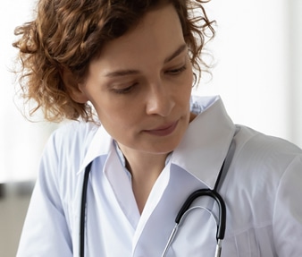 a nurse in white uniform i looking down a t laptop wearing a stethoscope