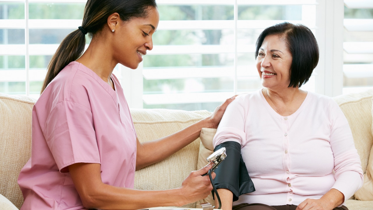 a nurse in pink hospital scrubs talks is taking a patient's blood pressure